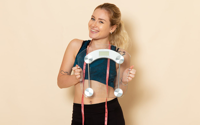 women holding weighing scale and an inch tape around her neck